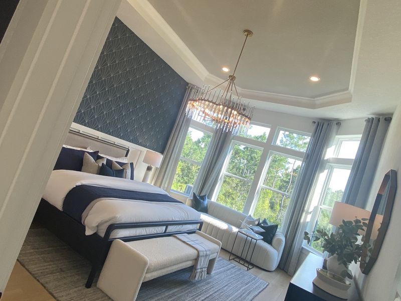 A luxurious bedroom with a bold accent wall, elegant chandelier, and ample natural light from large windows.