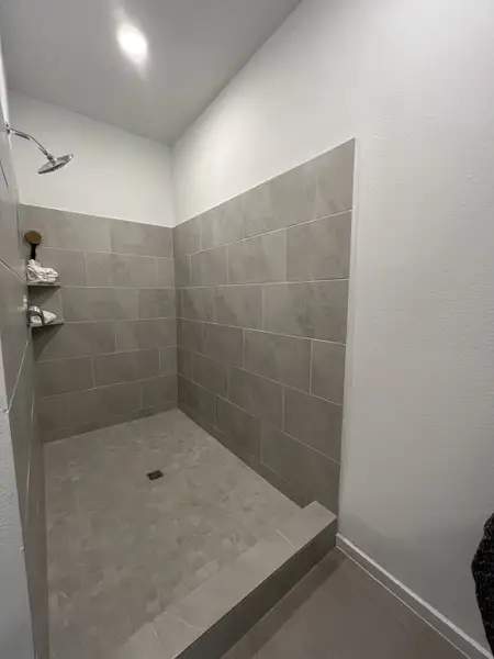 Modern shower with elegant gray tiles and a built-in shelf, featuring a minimalist aesthetic and bright lighting.