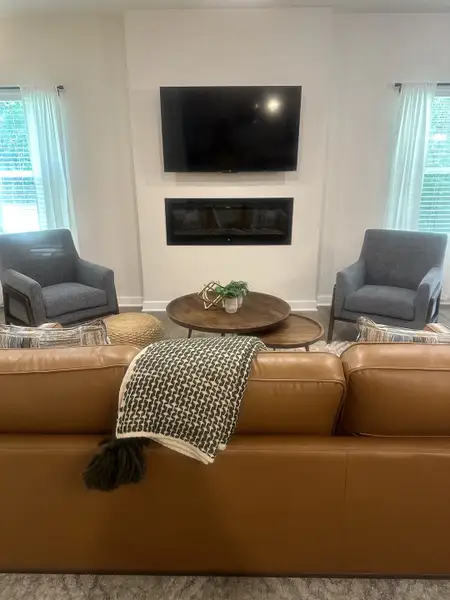 A cozy living room featuring a leather sofa, modern fireplace, TV, and stylish armchairs with bright natural lighting. A cozy living room featuring a leather sofa, modern fireplace, TV, and stylish armchairs with bright natural lighting.