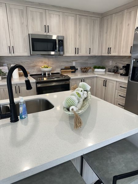 A modern kitchen with light wood cabinets, sleek countertops, stainless steel appliances, and stylish black fixtures.