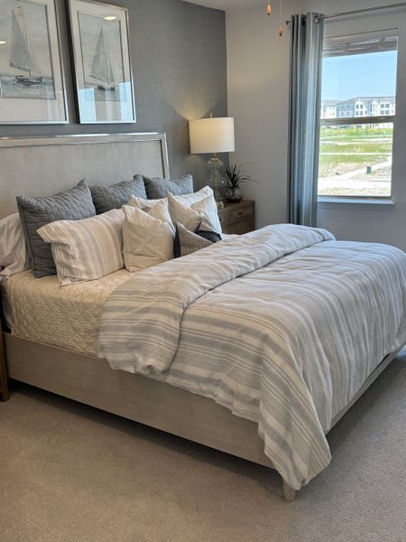 A cozy bedroom with a soft gray palette, framed sailboat art, and plush bedding.
