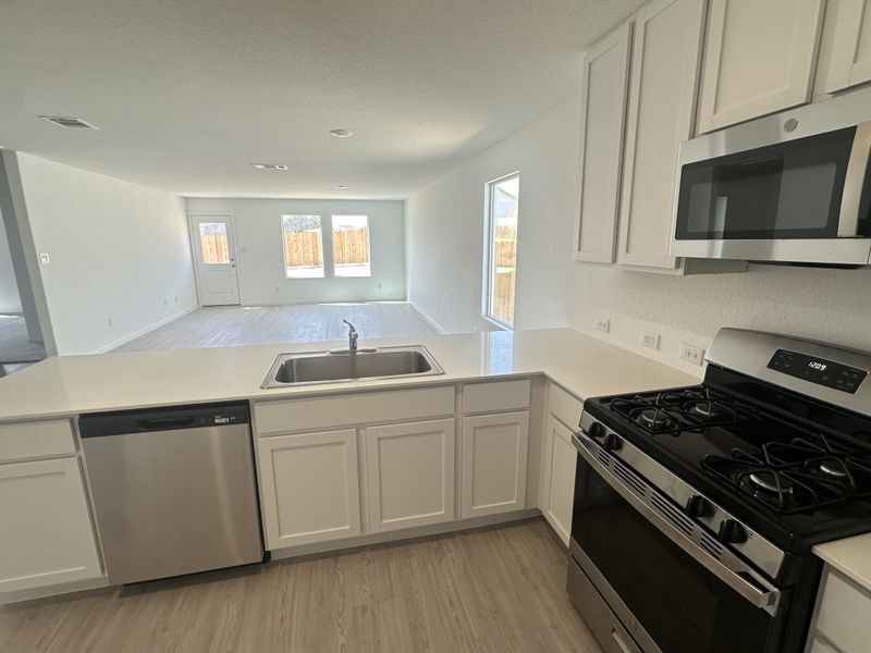 A modern kitchen with white cabinetry, stainless steel appliances, and an open floor plan leading to a bright living area.