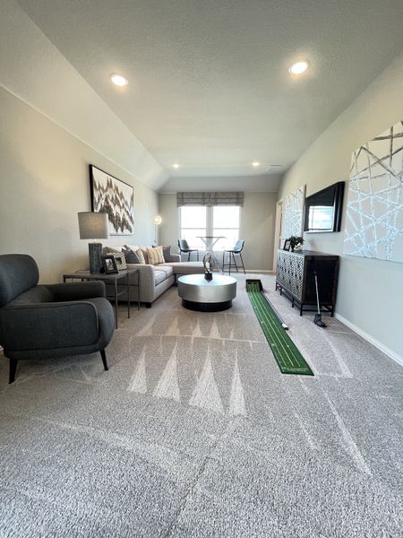 A contemporary living room with cozy seating, a putting green, and stylish wall art. Bright windows enhance the modern decor.