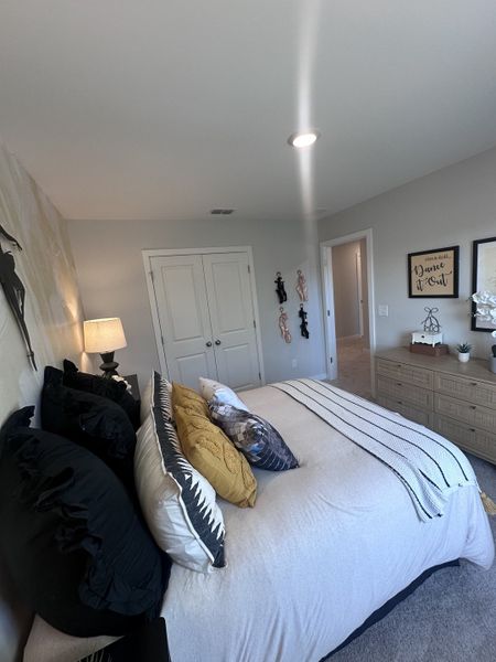 A cozy bedroom with modern decor, featuring a plush bed with assorted pillows, soft lighting, and a stylish dresser.