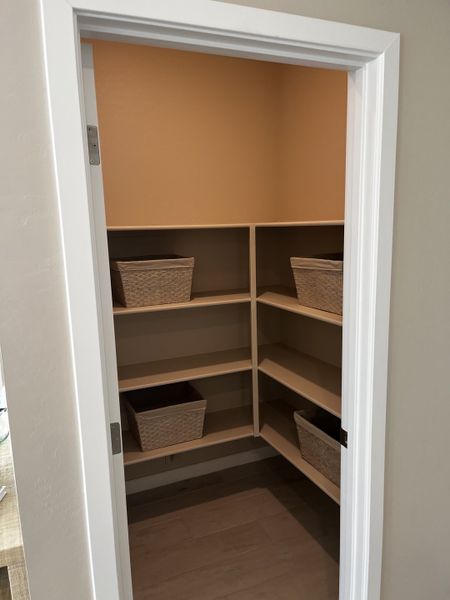 Neat pantry with wooden shelves and woven storage baskets, set against a warm beige wall.