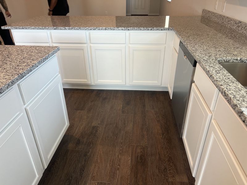 A modern kitchen featuring granite countertops, sleek white cabinetry, and rich wood flooring.