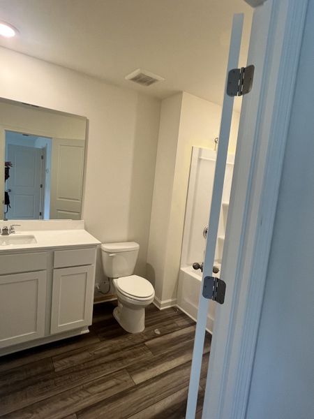 A contemporary bathroom featuring wood-look flooring, a sleek white vanity, and a streamlined shower area.