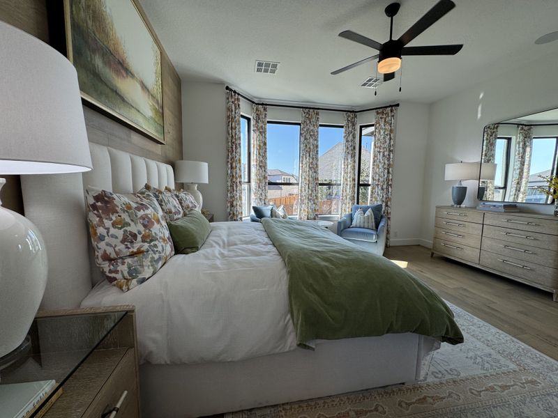A serene bedroom featuring a plush bed, floral accents, and elegant windows allowing ample natural light. A serene bedroom featuring a plush bed, floral accents, and elegant windows allowing ample natural light.