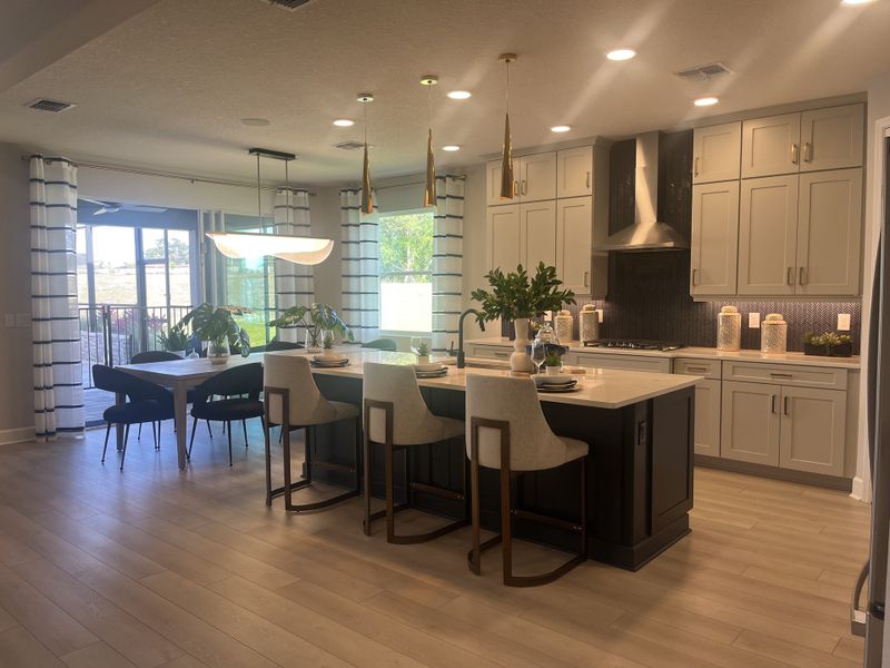 A modern kitchen with an expansive island, elegant lighting, and stylish dining area, featuring large windows and light wood flooring. A modern kitchen with an expansive island, elegant lighting, and stylish dining area, featuring large windows and light wood flooring.
