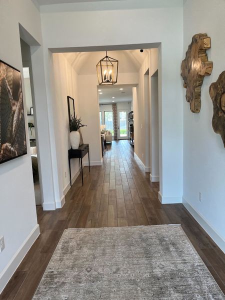 A bright hallway with wooden flooring, elegant lighting, and tasteful decor leads to an inviting living space.
