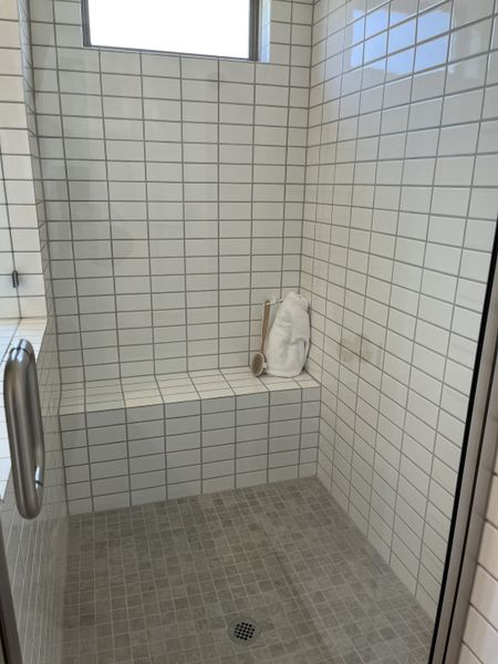 A sleek walk-in shower with white subway tiles, a built-in bench, and natural light peeking through a high window.