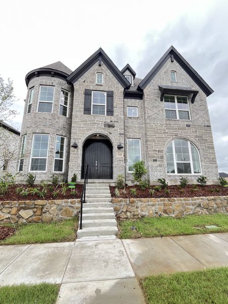 A beautiful brick home with elegant stone accents and landscaping in Edgewater by Grand Homes (Fate, TX).