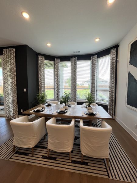 Modern dining room featuring a wooden table, white chairs, large windows with patterned curtains, and stylish decor. Modern dining room featuring a wooden table, white chairs, large windows with patterned curtains, and stylish decor.
