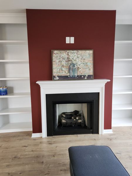 A cozy living area featuring a fireplace with a bold red accent wall and built-in white shelves.