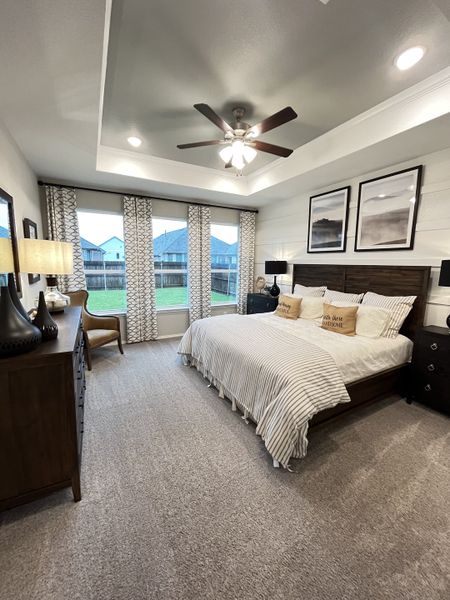 A cozy bedroom with plush carpeting, a wooden bed, and large windows framed by patterned curtains, creating a tranquil retreat.