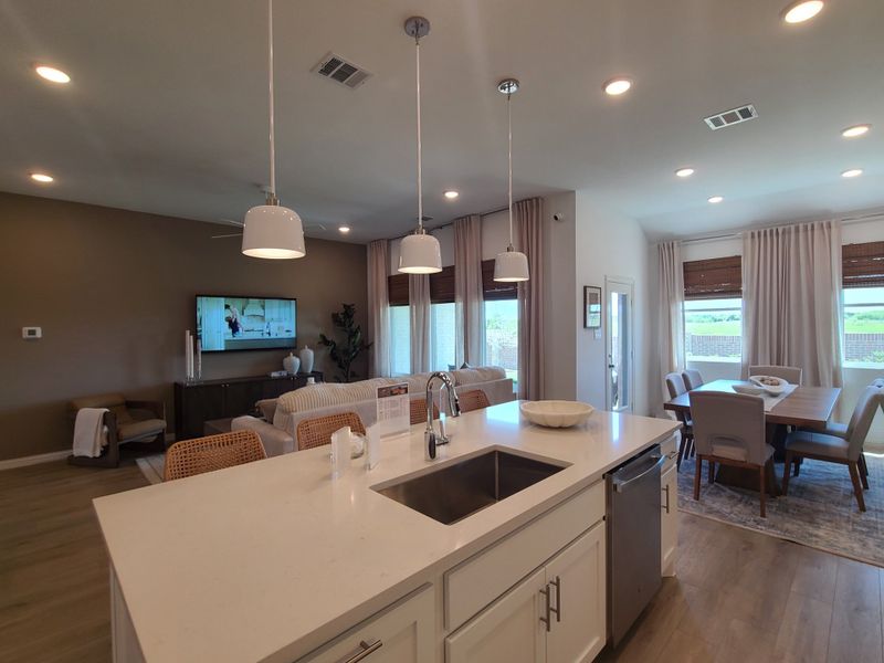 A modern, open-concept kitchen and living area with sleek lighting, cozy seating, and a dining space with large windows.