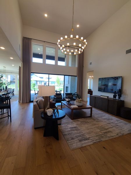 A spacious living area with high ceilings, a grand chandelier, modern furniture, and a large window for ample natural light. A spacious living area with high ceilings, a grand chandelier, modern furniture, and a large window for ample natural light.