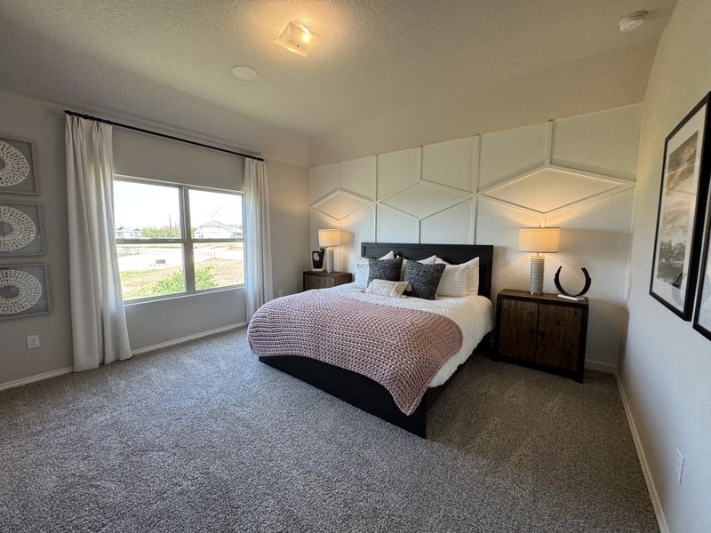 A cozy bedroom with geometric wall design, soft carpeting, and elegant decor featuring a large window for natural light.