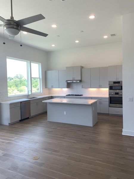 A modern kitchen with sleek gray cabinets, a central island, and stainless steel appliances. Bright with natural light.