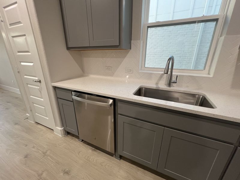 A modern kitchen with sleek gray cabinets, quartz countertops, and a stainless steel dishwasher.