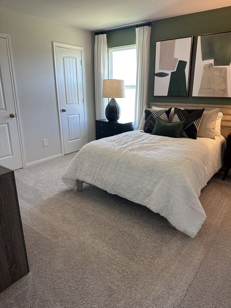 A cozy bedroom with a textured bedspread, abstract artwork, soft carpet, and natural light filtering through the window.
