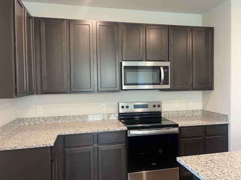 A modern kitchen with sleek dark cabinetry, granite countertops, and stainless steel appliances.