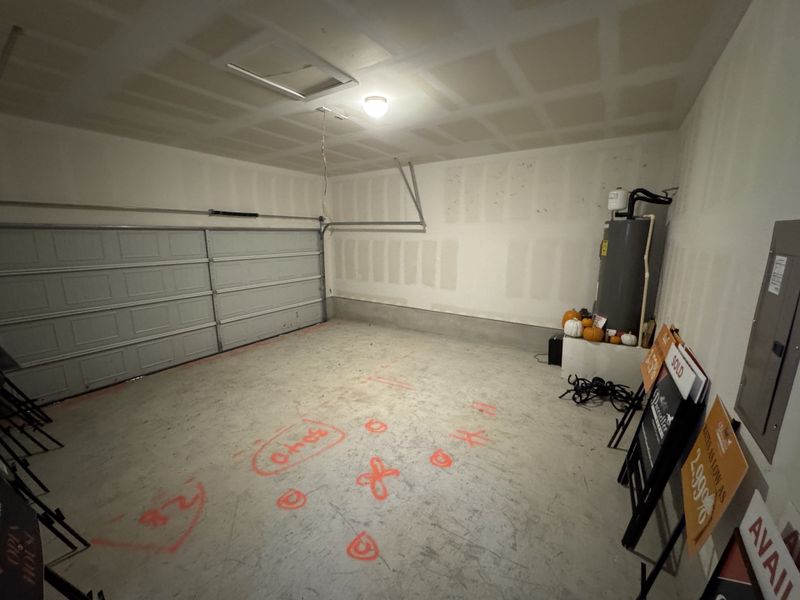 A spacious garage with unfinished walls, utility equipment, and storage signs neatly stacked in the corner.