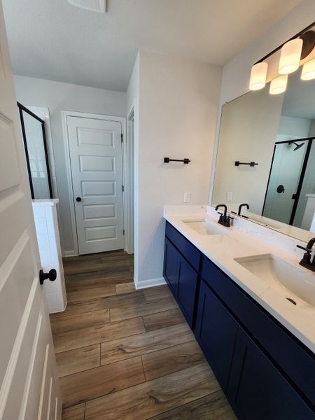 A sleek bathroom with dual sinks, dark blue vanity, elegant fixtures, and warm wood flooring.