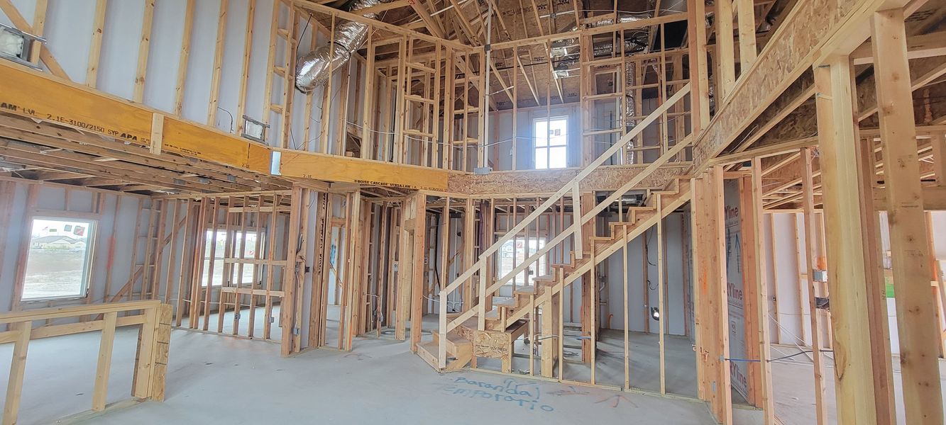 An under-construction home with exposed wooden framework, featuring a staircase and multiple windows.