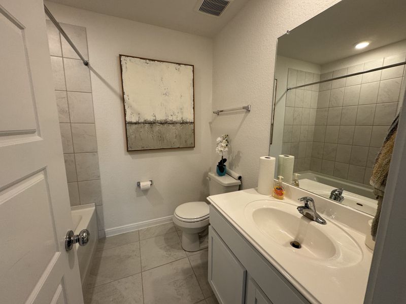 A bright bathroom with a simple vanity, tiled tub, modern artwork, and neutral tones creates a clean, minimalistic space.