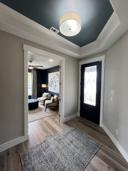A welcoming entryway with rich wood floors, elegant ceiling design, and bright natural light leading to a cozy sitting room. A welcoming entryway with rich wood floors, elegant ceiling design, and bright natural light leading to a cozy sitting room.