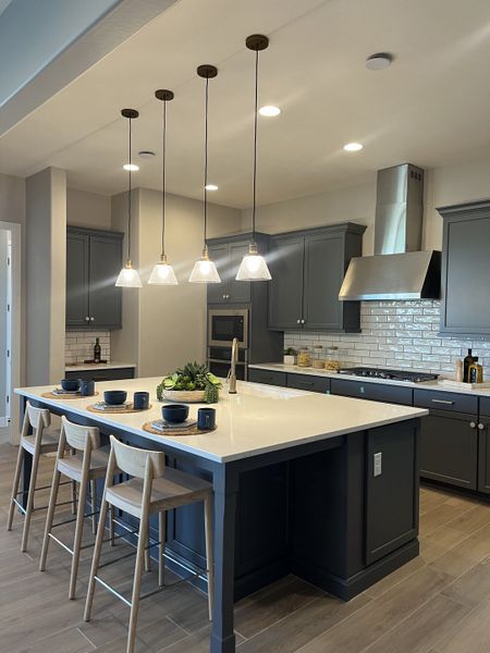A modern kitchen with sleek gray cabinets, an elegant island, and pendant lighting.