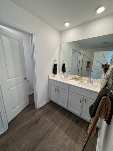 A sleek bathroom featuring dual sinks, white cabinetry, and rich wood floors for a modern touch.