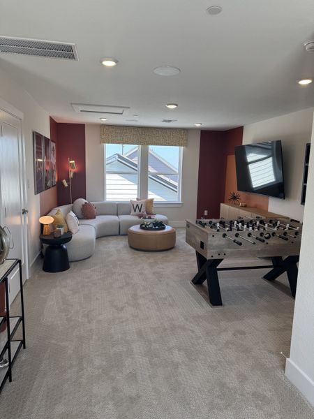 A cozy rec room with a curved sofa, foosball table, and mounted TV, perfect for relaxation and entertainment.