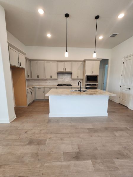 A modern kitchen with light wood flooring, sleek cabinetry, and an island with pendant lighting.