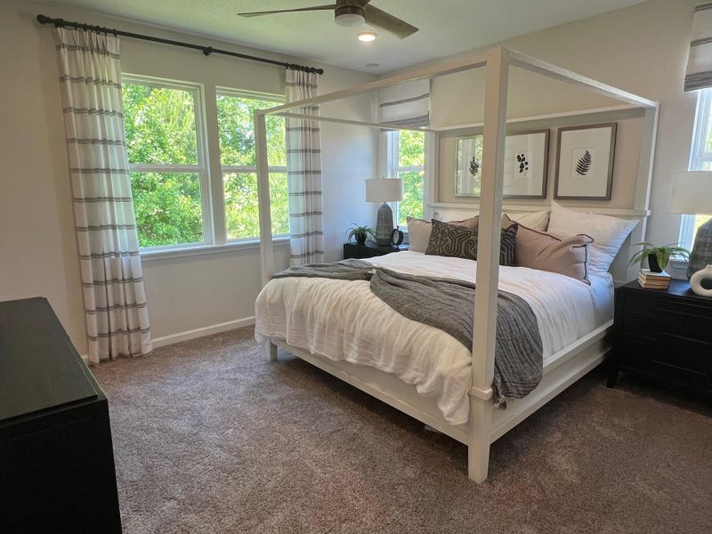 A cozy bedroom featuring a four-poster bed, neutral decor, and large windows overlooking greenery.