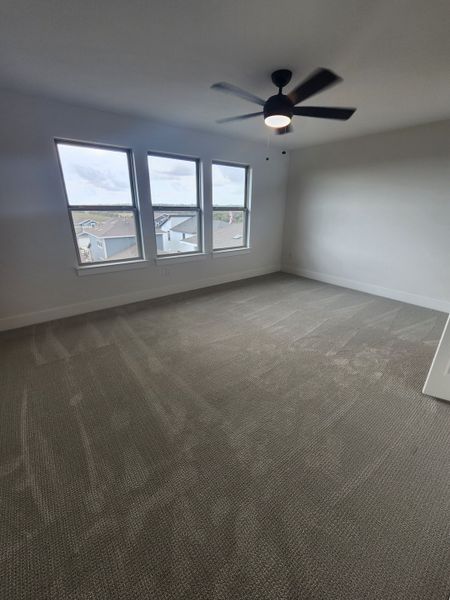 A spacious bedroom with soft carpet, large windows, and a modern ceiling fan.