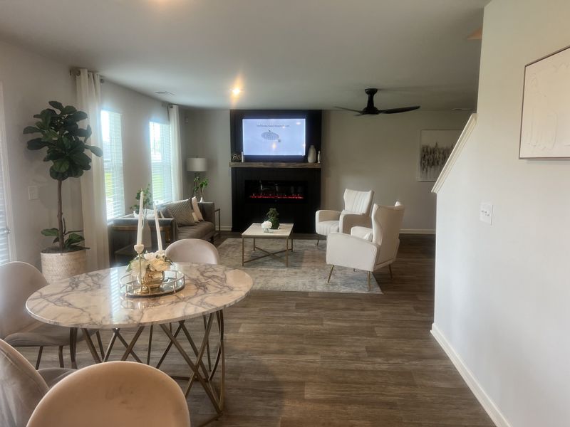 Modern living room with a marble dining table, cozy seating, wood floors, and a stylish fireplace with a mounted TV.