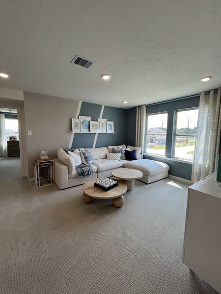A cozy living room with a plush sectional, wooden coffee tables, and large windows providing ample natural light.