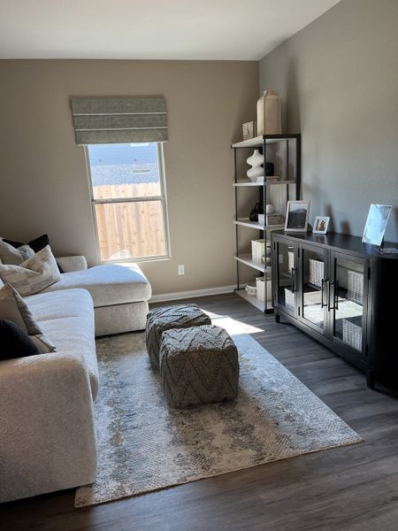 A cozy living room with a plush sectional, decorative ottomans, and a sleek cabinet in neutral tones.