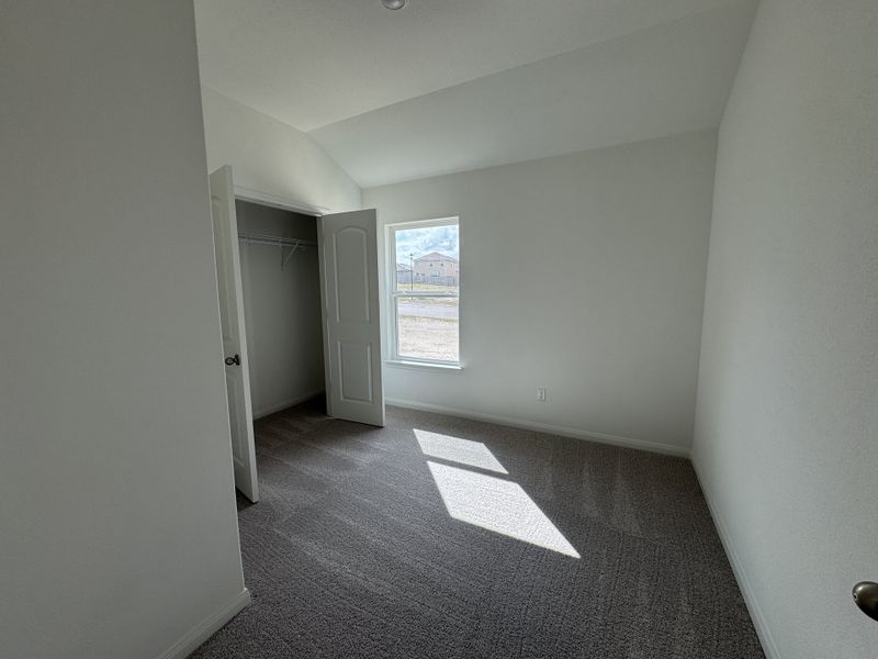 A sunlit room with plush carpeting, neutral walls, and a walk-in closet, perfect for a cozy and inviting atmosphere.