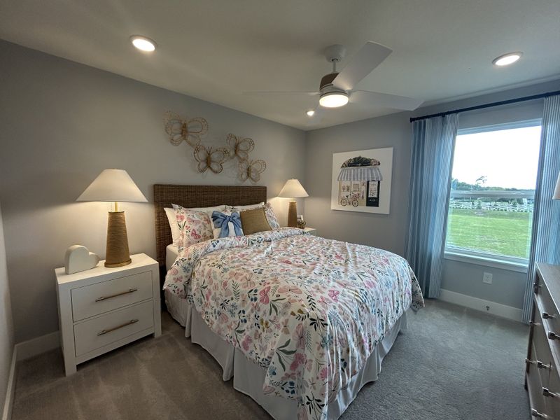 A cozy bedroom with floral bedding, soft lighting, and a large window offering scenic views.
