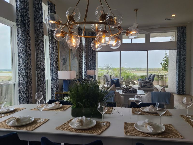 A chic dining area with a sleek chandelier, elegant table setting, and expansive view of the outdoors through large windows. A chic dining area with a sleek chandelier, elegant table setting, and expansive view of the outdoors through large windows.