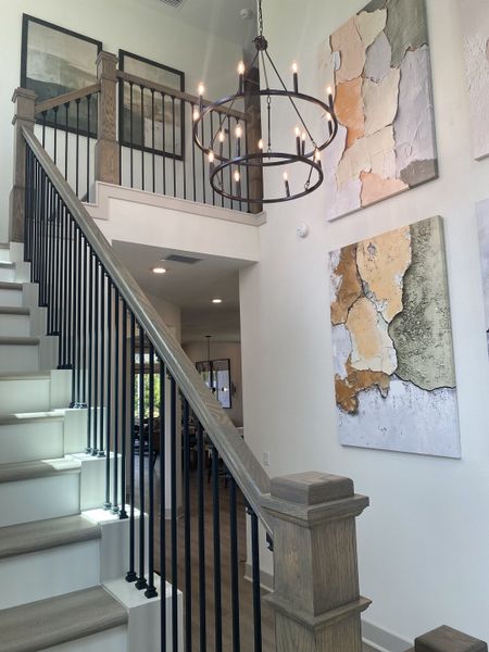 A contemporary stairway with wood accents, modern art, and an elegant chandelier creates a stylish and inviting entryway.
