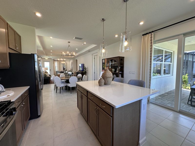 A modern open kitchen and dining space with sleek lighting, island seating, and sliding doors to the patio.