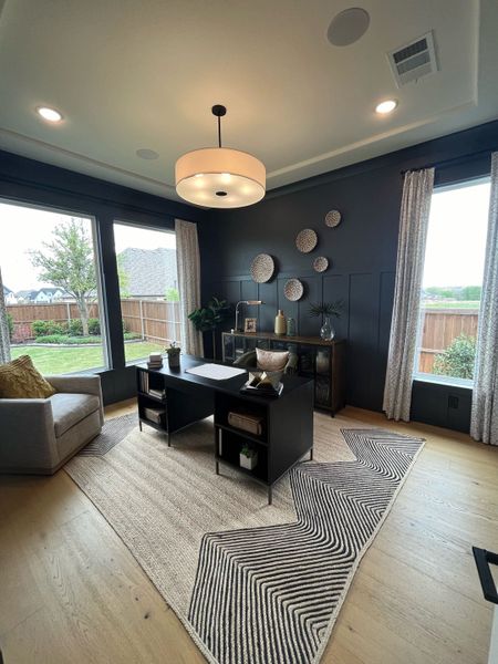A stylish home office with dark walls, a modern desk, large windows, and elegant decor.
