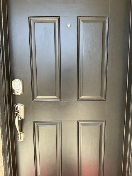 A sleek black door with elegant paneling and a modern silver handle, featuring a smart lock and peephole.