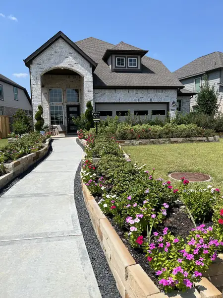 A beautiful brick home with manicured gardens and a curved walkway in Dellrose by Chesmar Homes (Hockley, TX).