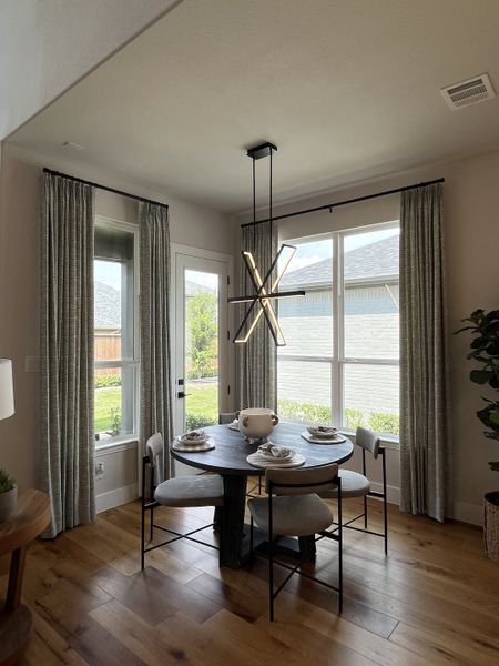 A cozy dining nook with a round table, modern chandelier, and large windows with flowing curtains.