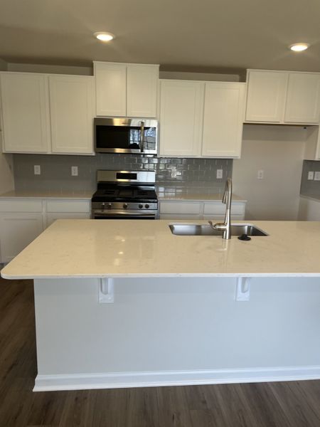 A modern kitchen with white cabinets, stainless steel appliances, and a spacious island with a sleek finish. A modern kitchen with white cabinets, stainless steel appliances, and a spacious island with a sleek finish.